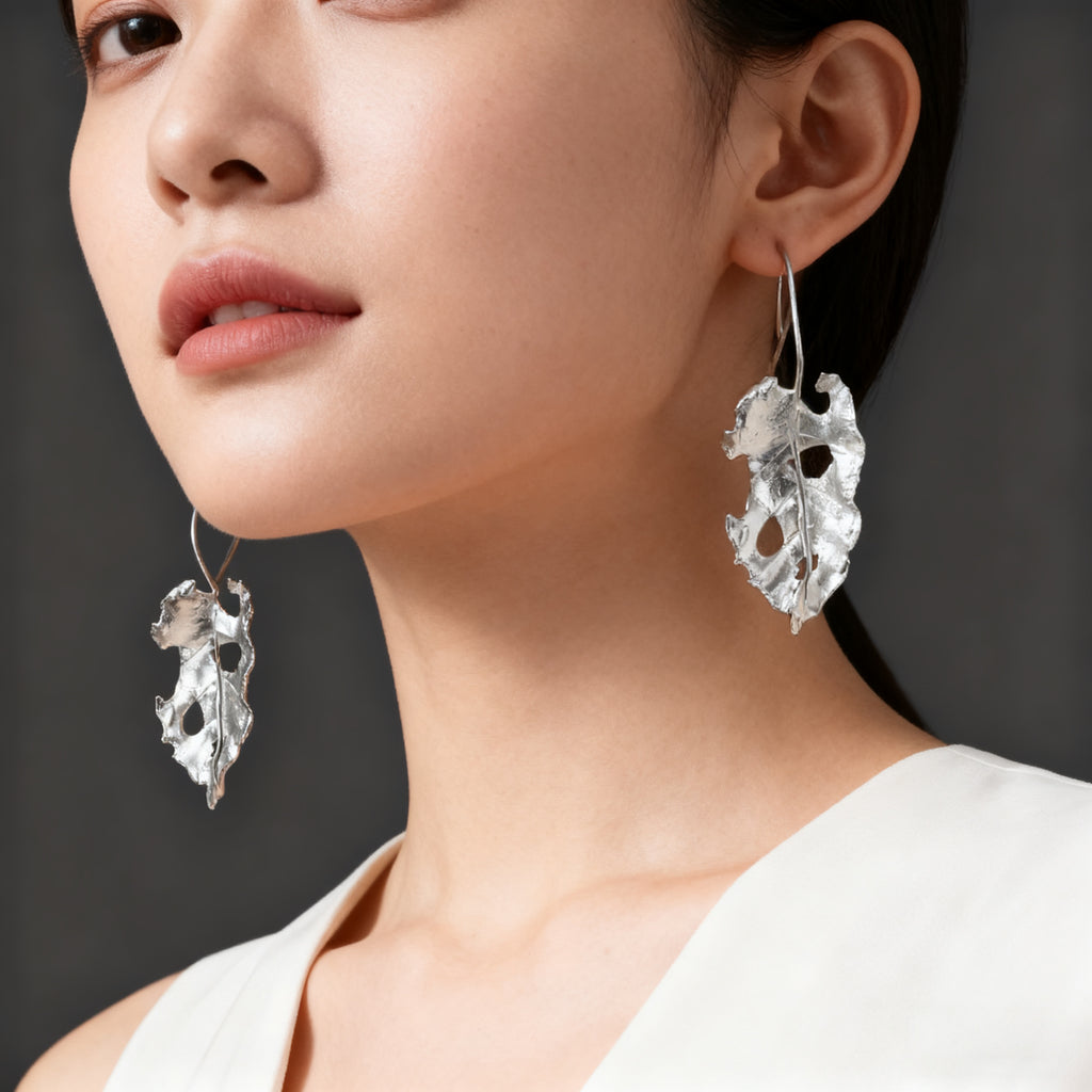 Artistic silver earrings inspired by natural leaf forms with sculpted, irregular texture.
