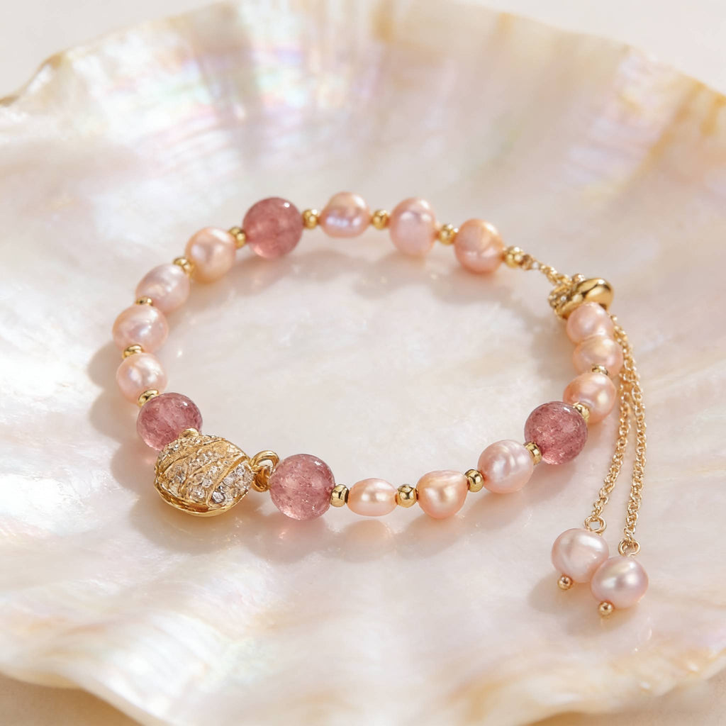 An adjustable bracelet featuring pink freshwater pearls, translucent pink beads, and a gold locket-style seashell charm placed on iridescent shell textures.
