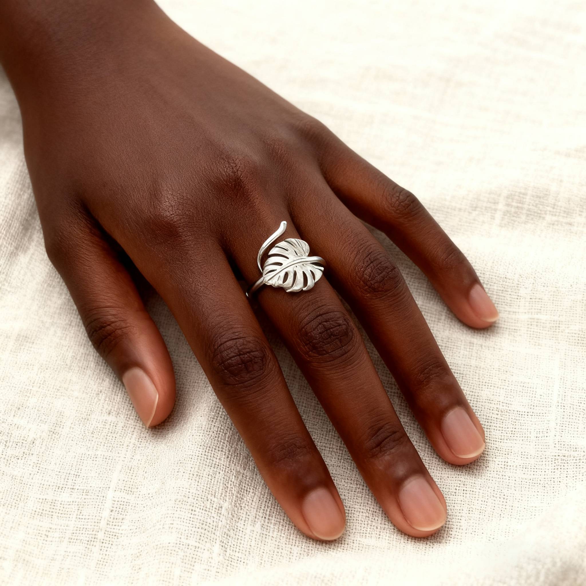 Handmade silver monstera leaf ring with adjustable band, styled on natural fabric background.