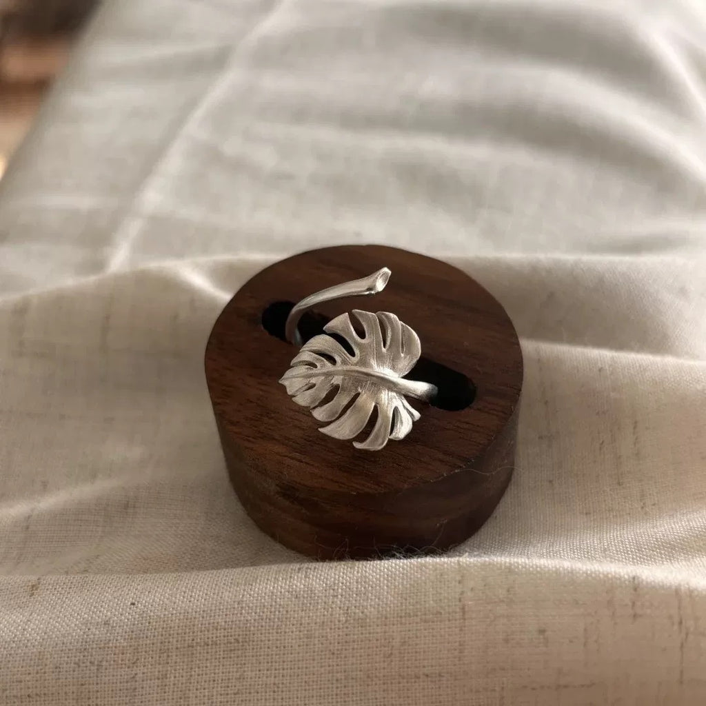 Minimalist silver ring featuring a handcrafted monstera leaf design, displayed on a wooden stand.