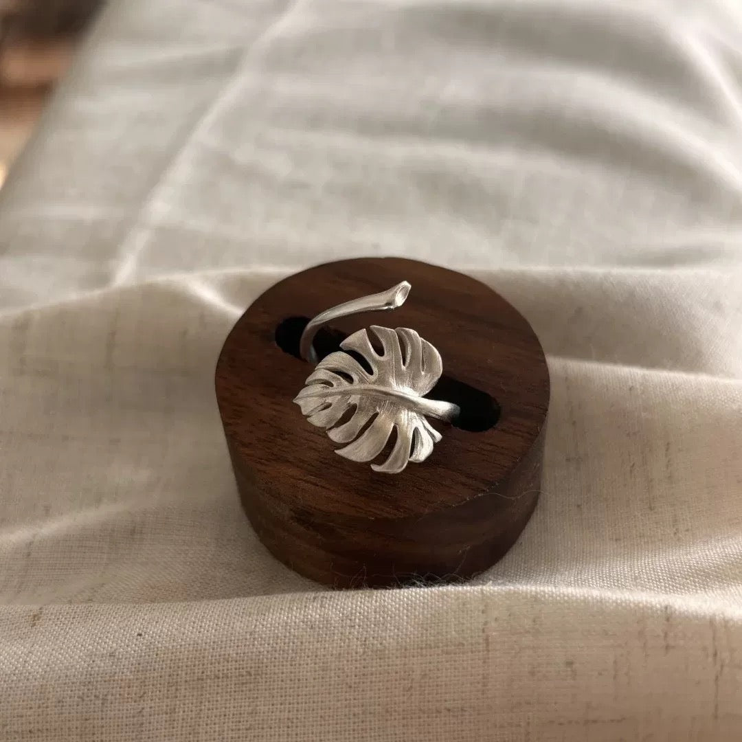 Minimalist silver ring featuring a handcrafted monstera leaf design, displayed on a wooden stand.