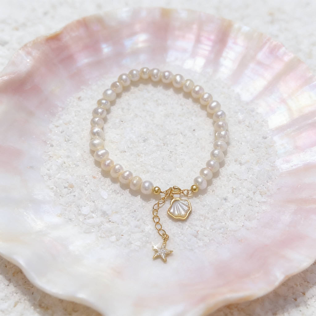 Pearl bracelet with gold charm on a seashell background