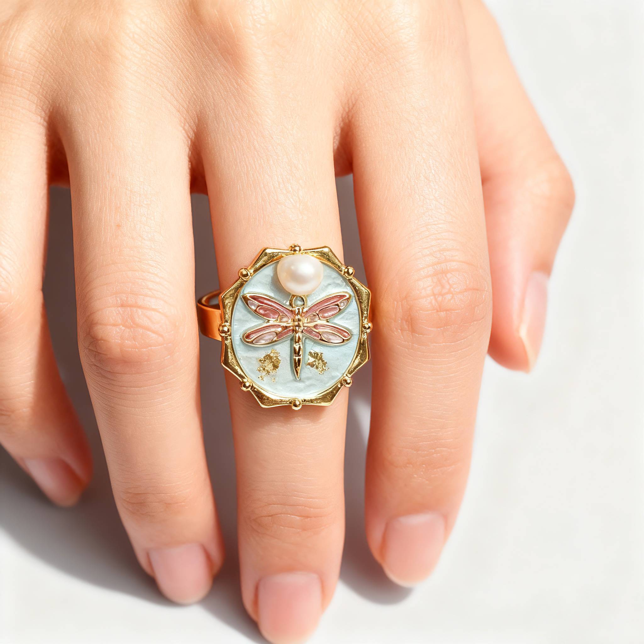 Ring with dragonfly design on a finger against a white background