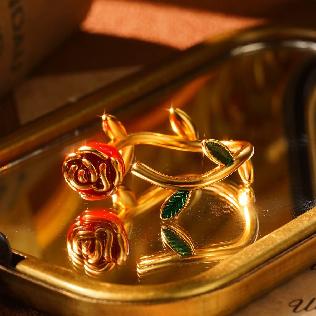 Gold rose ring with red enamel flower and green leaves, designed with an adjustable open band and vintage floral style.