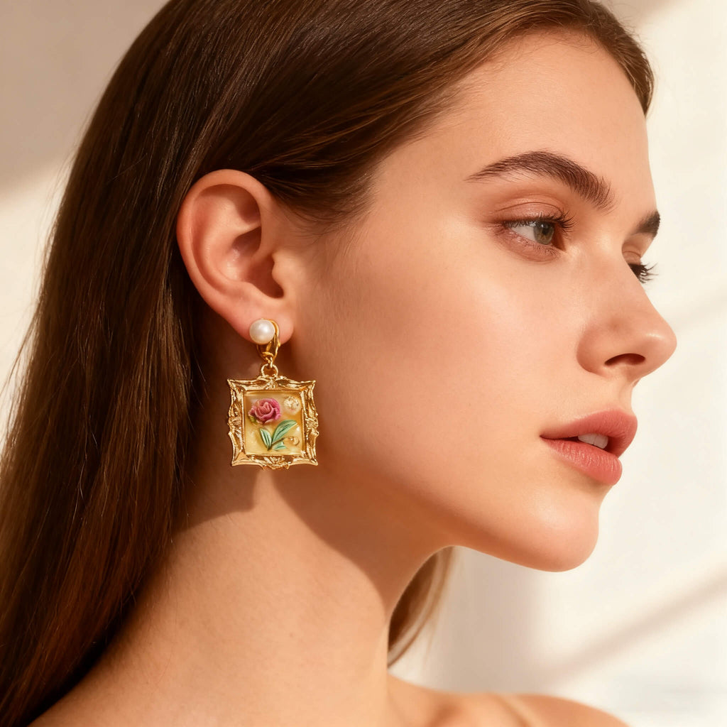 Baroque-style gold frame earrings featuring delicate floral painting, displayed in warm holiday lighting.