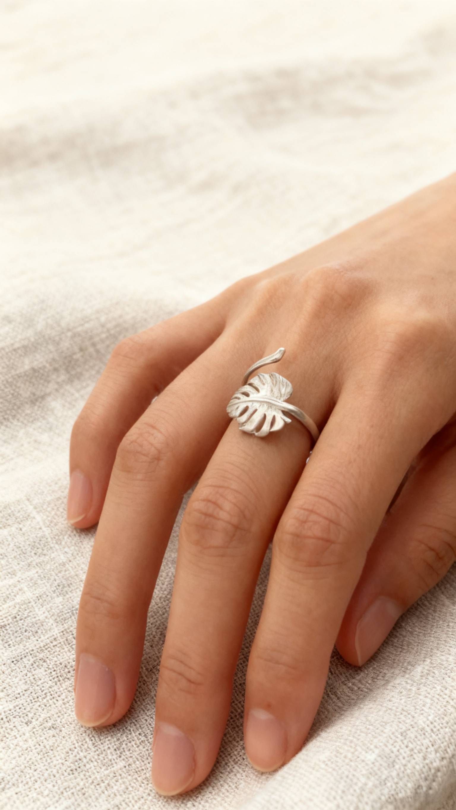 Nature-inspired silver monstera leaf ring with organic texture, photographed against soft neutral fabric.