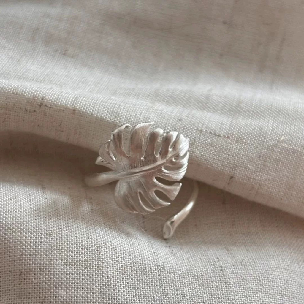 Elegant silver ring shaped like a detailed monstera leaf, presented on a wooden display base.