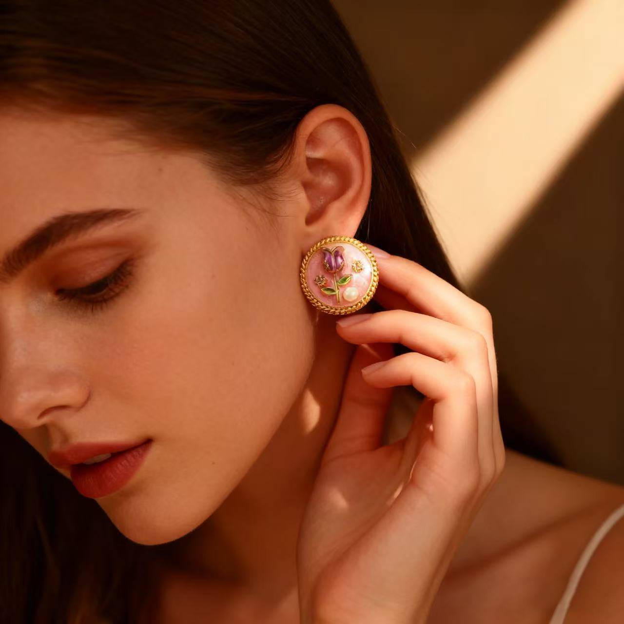 Elegant round gold earrings featuring a pink enamel rose, green leaves, and shimmering details.