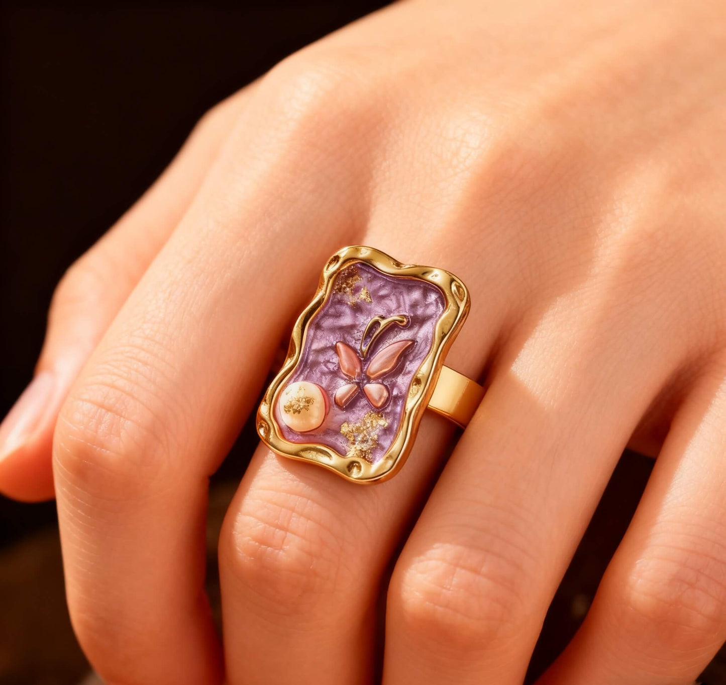 Close-up of a gold butterfly ring with shimmering purple enamel and pearl detail.