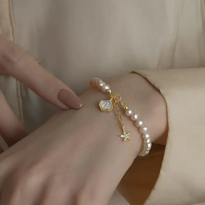Pearl bracelet with gold charm on a wrist against a neutral background