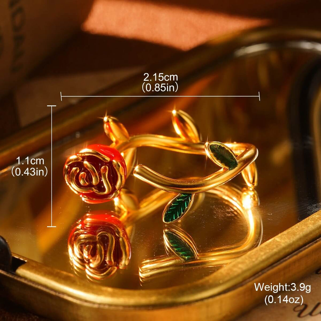 Elegant gold rose ring featuring a red enamel blossom and green leaf accents, reflecting warm light for a romantic jewelry look.