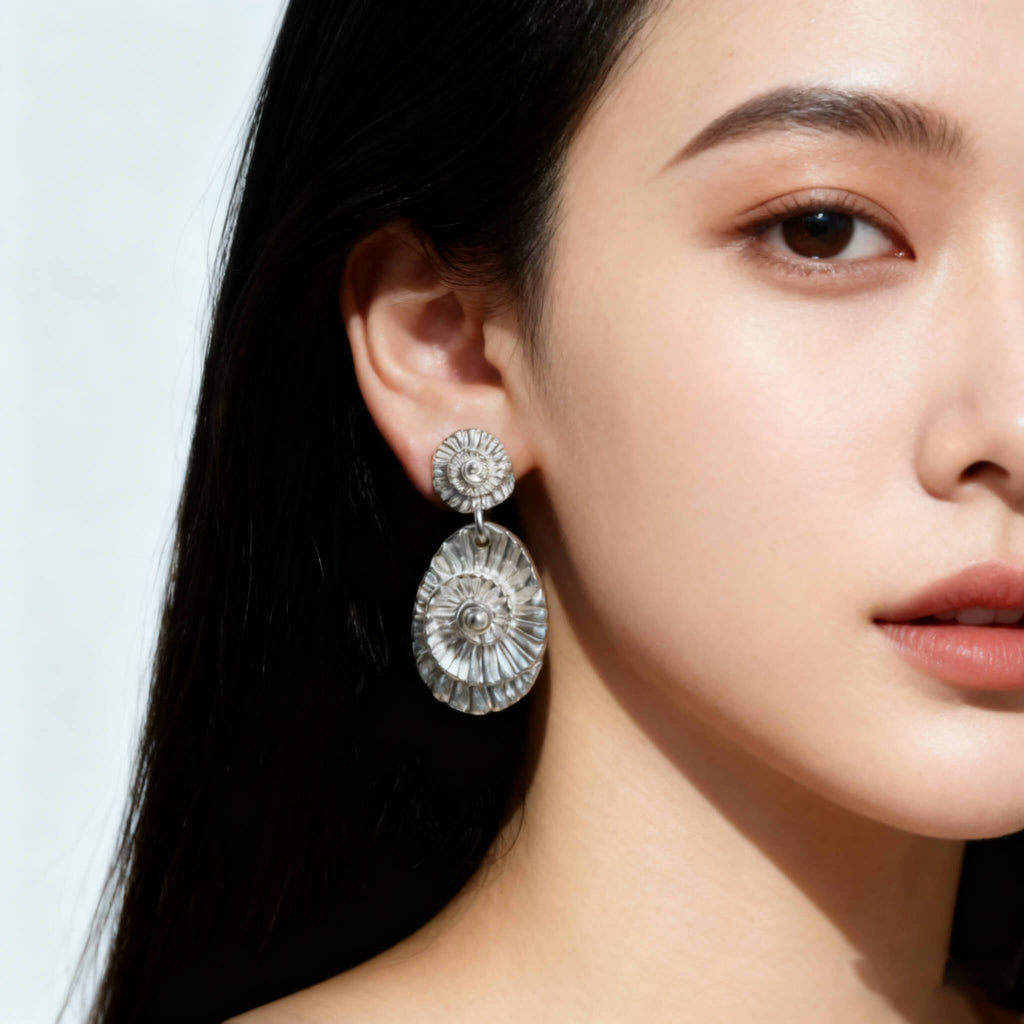 Elegant silver earrings inspired by seashell shapes with detailed ridges.