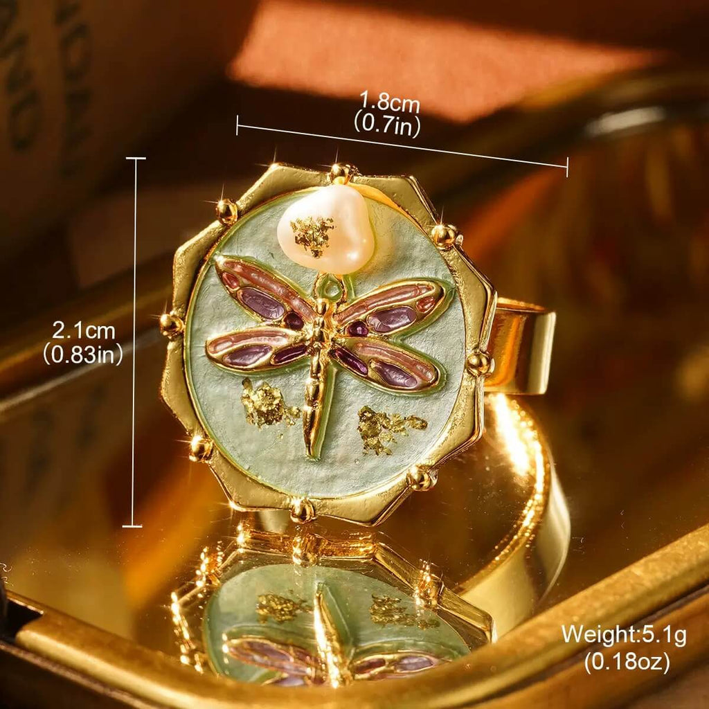 Elegant gold dragonfly ring with mother-of-pearl base and decorative pearl top, styled under warm light.