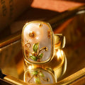Close-up of a gold ring with a pearl flower and green leaf details.